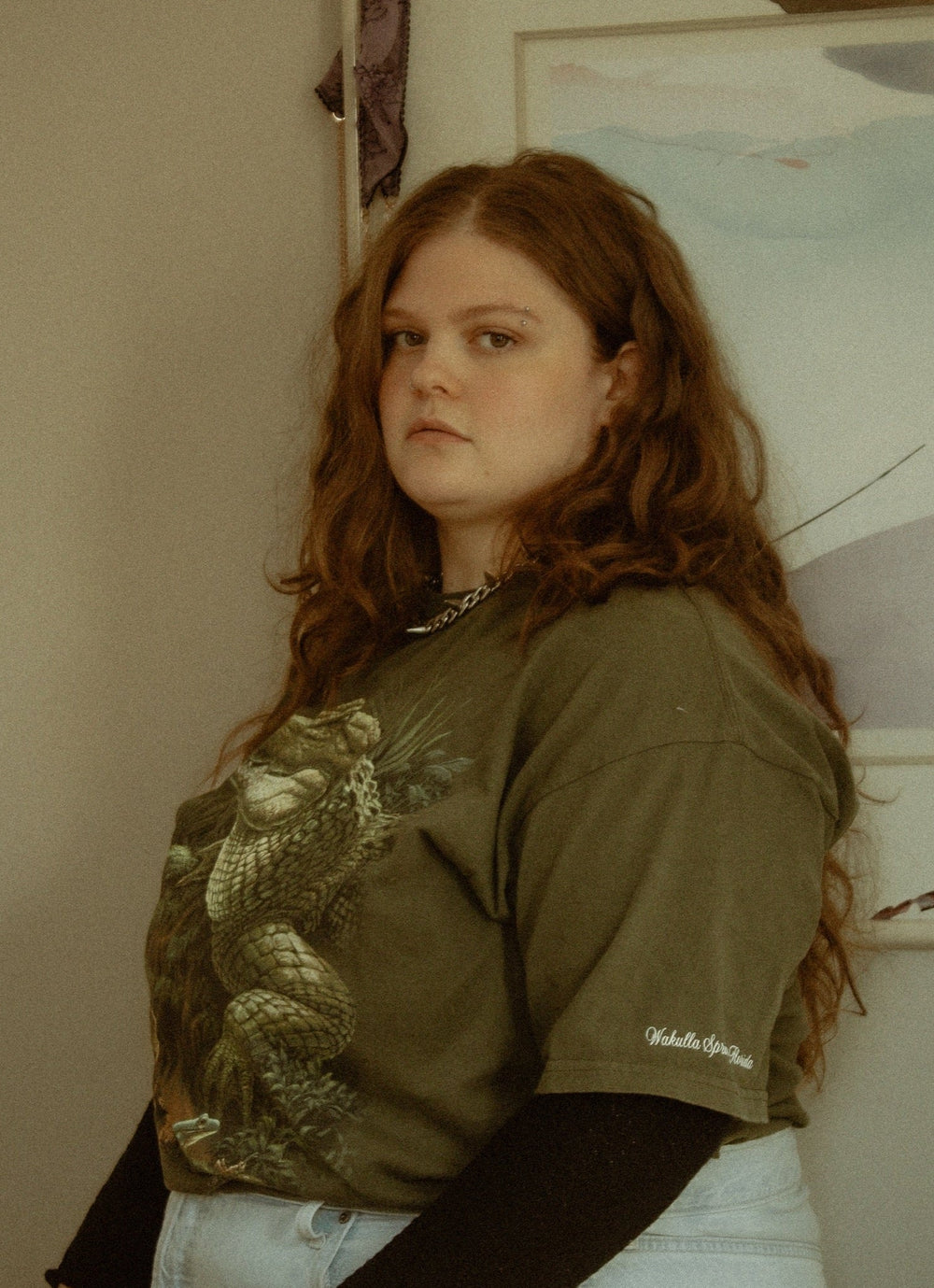 a nonbinary person sits in a green shirt and jeans shorts with their hands on their legs